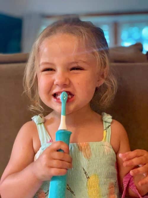 Young girl brushing teeth in room. 